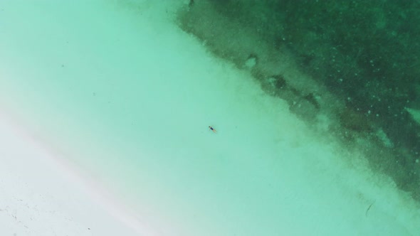 Aerial: woman swimming in turquoise water at sunset white sand beach tropical coastline