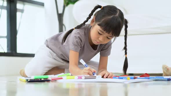 Cute adorable asian ethnic kid girl holding color pen drawing and painting, lying on warm floor