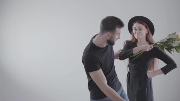 Elegant Offended Caucasian Girl in Black Dress and Hat Beating Her Boyfriend or Husband with Flowers