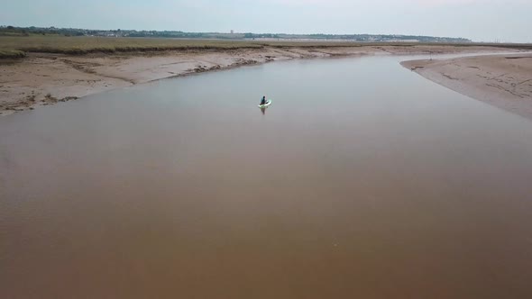 Man kayaking on meandering river, drone pans up to reveal beautiful landscape in the background.