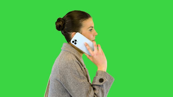 Young Woman in Stylish Clothes Walks Talking on Mobile Phone on a Green Screen Chroma Key