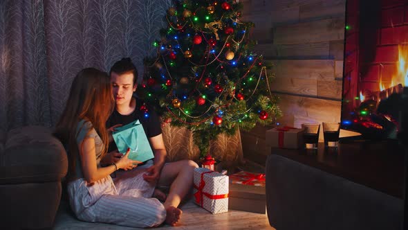 Young Couple Sitting on the Floor and Exchanging Gifts on Christmas