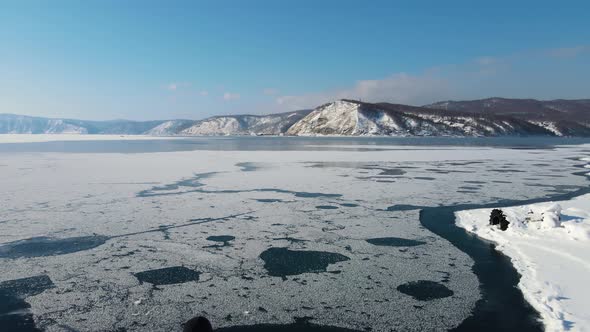 A traveller with a backpack sits on snow of a river shore. Drone footage