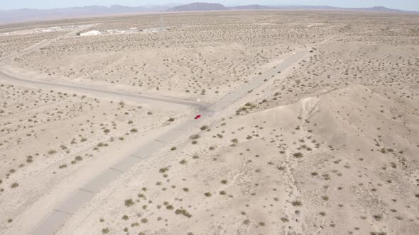 Aerial view following a red car driving through the desert