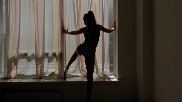 The Silhouette of a Sexy Woman in Striptease Shoes Who Dances Near a Window