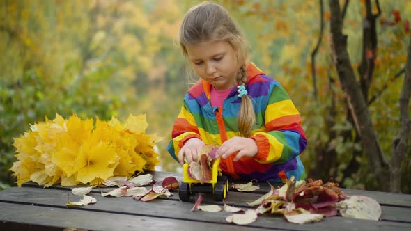 A little girl playing with a toy car on an autumn day.