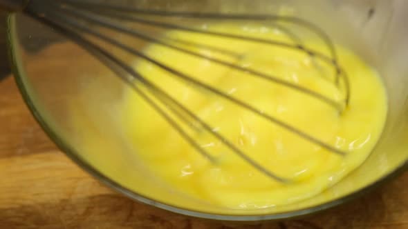 Person preparing homemade omelette mixing with whisk eggs. Close up.HD