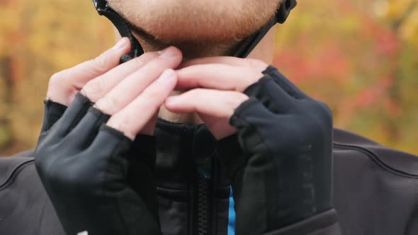 Professional male cyclist closing zipper on jacket and helmet clasp before outdoors cycle training