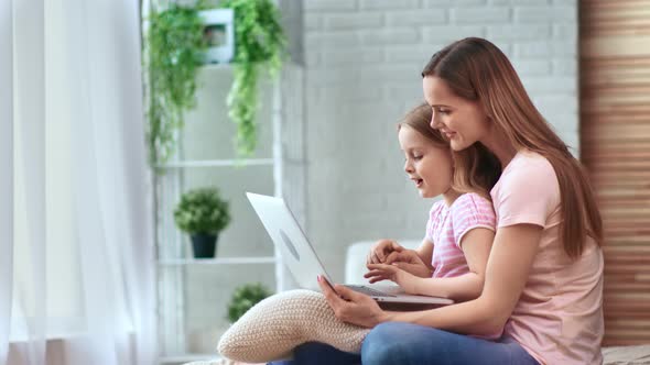 Positive Blonde Female and Pretty Child Use Computer Sitting on Bed