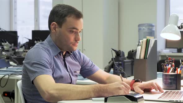 Professional Creative Man Sitting at His Desk in Home Office Studio Working on a Laptop Writes