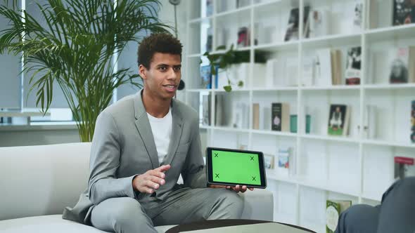 Black Formal Man Making Presentation with Tablet with Green Chromakey Screen. Young African-American