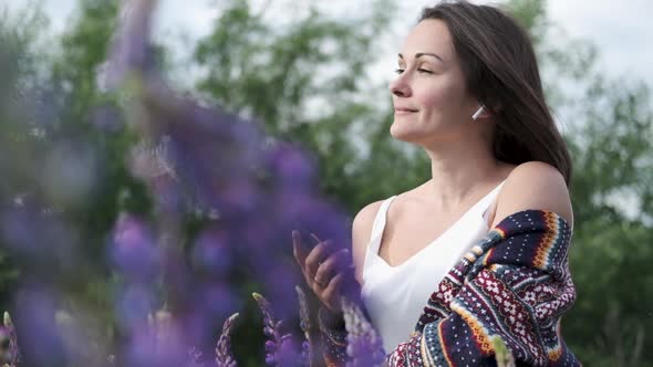 Beautiful Young Woman in Wireless Headphones Dancing in a Field of Flowers. Happy Girl Dancing in