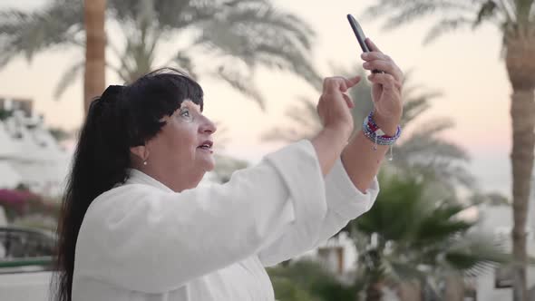 Smiling Caucasian Senior Woman Making Selfie on Smartphone. It Should Be on the Terrace of the Hotel