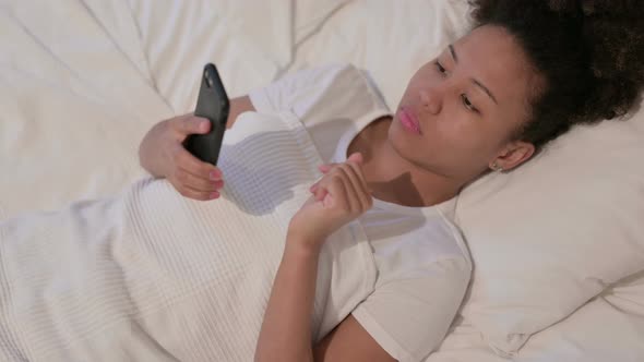 African Woman Using Smartphone While Sleeping in Bed