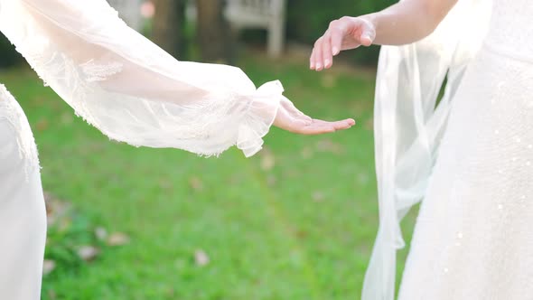 4K Portrait of Asian lesbian couple in wedding dress holding hands walking together in the garden.