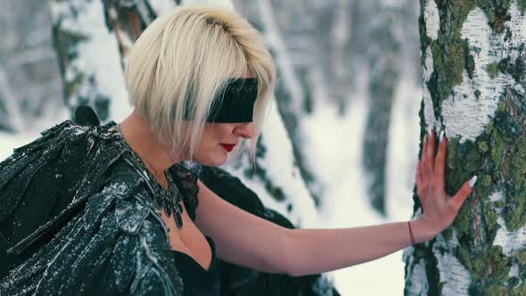 Woman in Phoenix Suit with Blindfold Leans on Tree in Forest