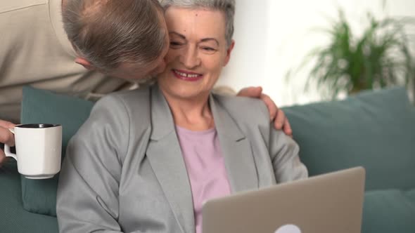 Mature Woman with Short Gray Hair is Working with Laptop While Sitting on Sofa at Home