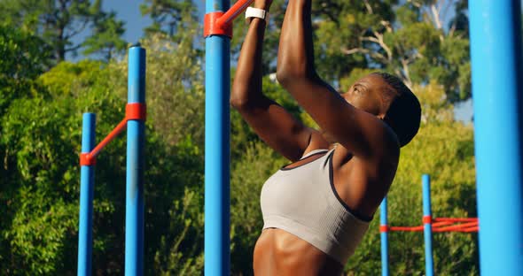 Female athlete exercising pull up on a pull up bar in the park