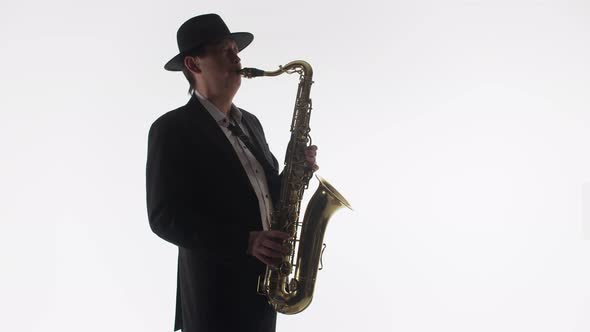 Man Saxophonist Plays the Saxophone in the Studio on a White Background and in Dark Light