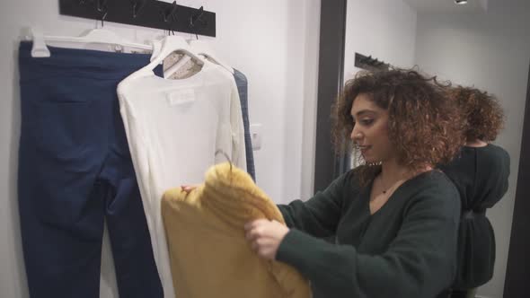 Woman in Clothes Store's Changing Room Looking at Clothes