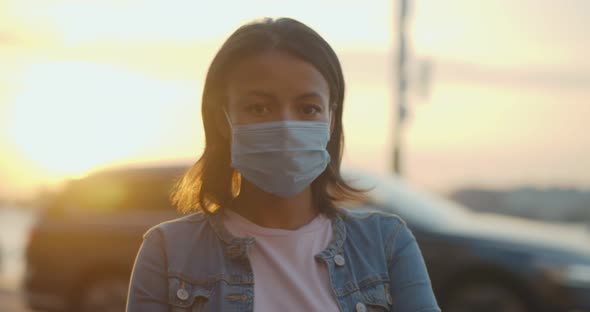 Bokeh Shot of Black Woman Wearing Protective Face Mask Looking at Camera Outdoors