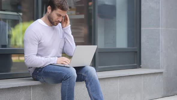Tense Handsome Man with Headache Working on Laptop Sitting Outside Office