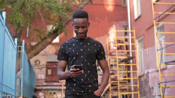 A young guy walks along the street in the city ghetto and looks at the phone