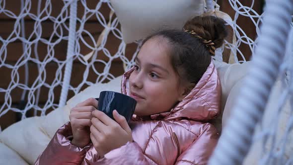 Teenage Girl with a Beautiful Model Face is Drinking Tea in a Street Chair