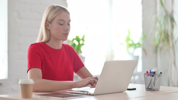 Young Blonde Woman Smiling at Camera while using Laptop in Office