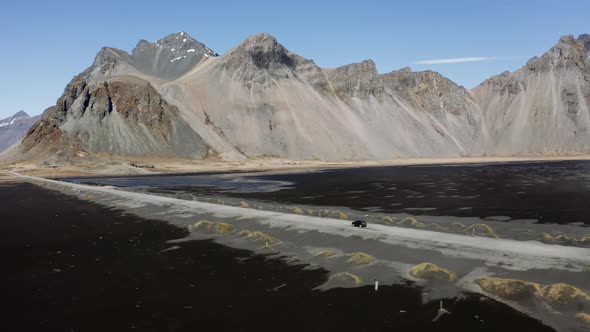 Drone Of Car Driving Along Narrow Road At Low Tide Towards Vestrahorn