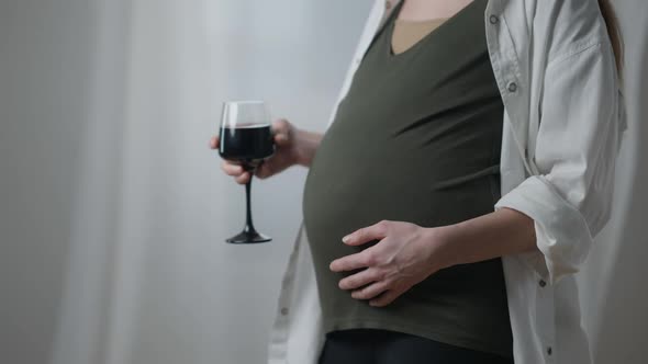 Young Unrecognizable Pregnant Woman with Glass of Red Wine Standing Indoors Shaking Drink
