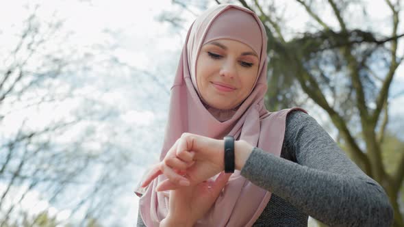 Attractive Muslim Woman in Sport Clothes and Hijab Checking Pulse on Smart Watch