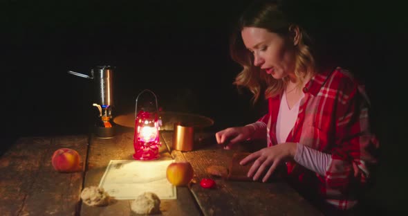 Woman Is Cutting Bread at Camping Site with Bright Orange Bonfire on Background alt