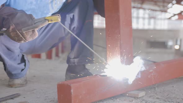 A man in a blue working uniform, in leather brown gloves, performs welding work