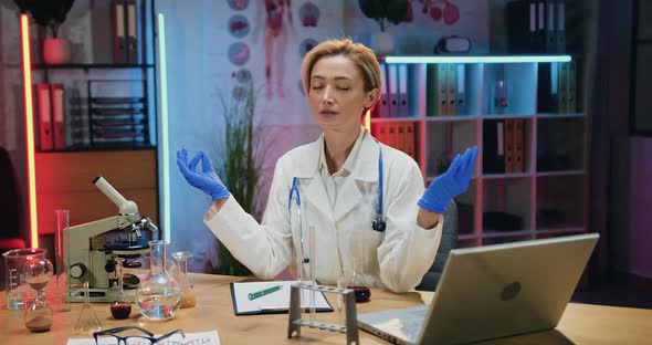 Doctor Meditating with Closed Eyes and Mudra Hands in Modern Medical Workroom in the Evening