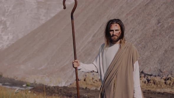Jesus Christ with a Staff in Robe is Standing on the Mountain and Looking Far
