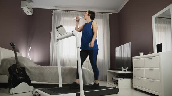 Attractive girl is drinking water during workout training on treadmill at home