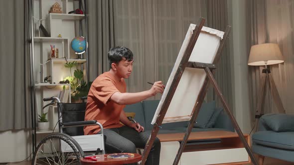 Asian Artist Boy In Wheelchair Holding Paintbrush And Thinking Before Painting On The Canvas