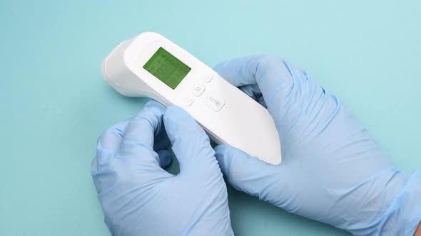 hand in blue latex gloves hold an electronic thermometer to measure temperature