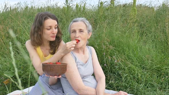 Senior Mother with Gray Hair with Her Adult Daughter in the Garden Hugging Each Other During Picnic