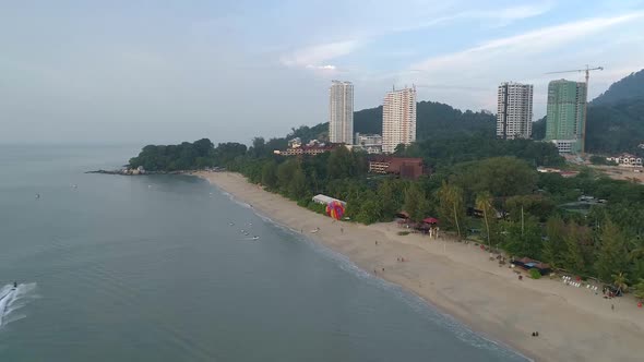 A drone shot of a parasailer behind the boat landing on the beach Batu Feringghi in  Penang, Malaysi