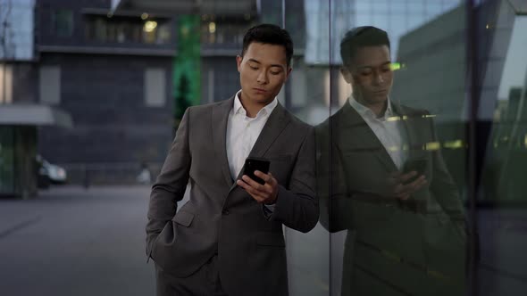 Real Time Shot of a Young Asian Businessman Conducting Business Correspondence, Standing Leaning