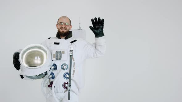 Astronaut with Helmet in His Hand on Light Background Waves with His Other Hand