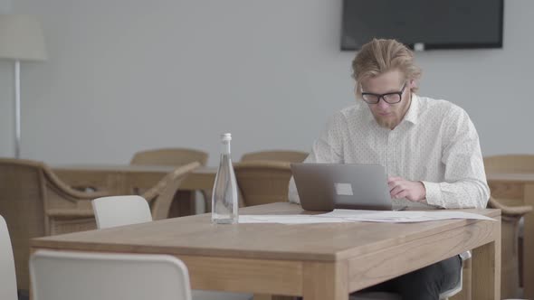 Portrait Successful Blond Thoughtful Man in Glasses Sitting at the Table