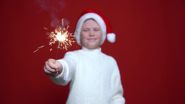 Happy Little Boy in Santa Claus Cap Holding Bengal Light on the Red Background