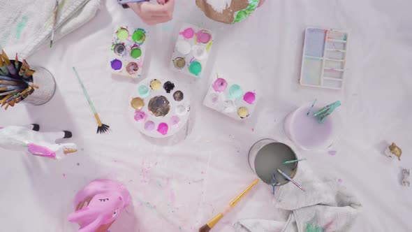 Flat lay. Little girl painting paper mache figurines with acrylic paint  for her homeschooling art p