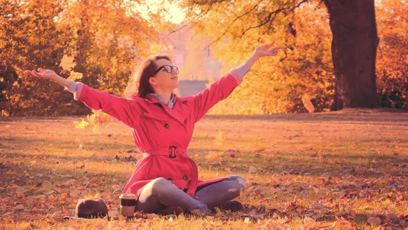 Woman in Red Cloak Throwing Autumn Leaves in Park