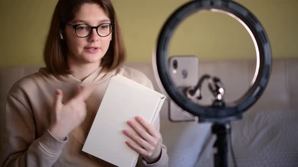 Girl book blogger with eye glasses recording vlog on digital smartphone cam
