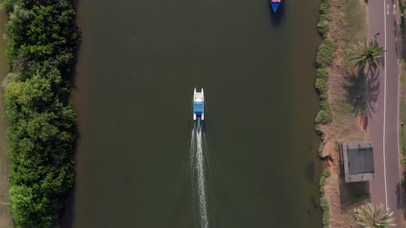 Small White boat heading upstream of the Yarkon river passing under city bridges.