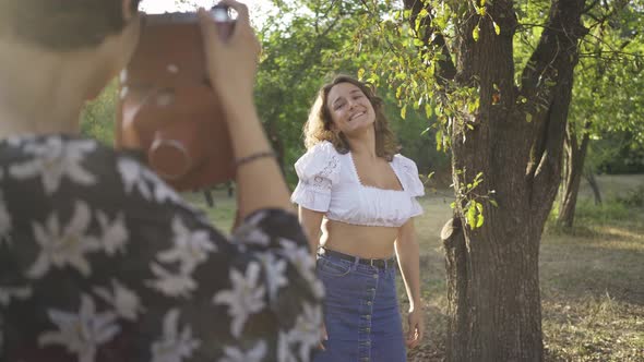 Caucasian Woman with Curly Hair Posing in Background While Her Friend Taking a Photo Using Old